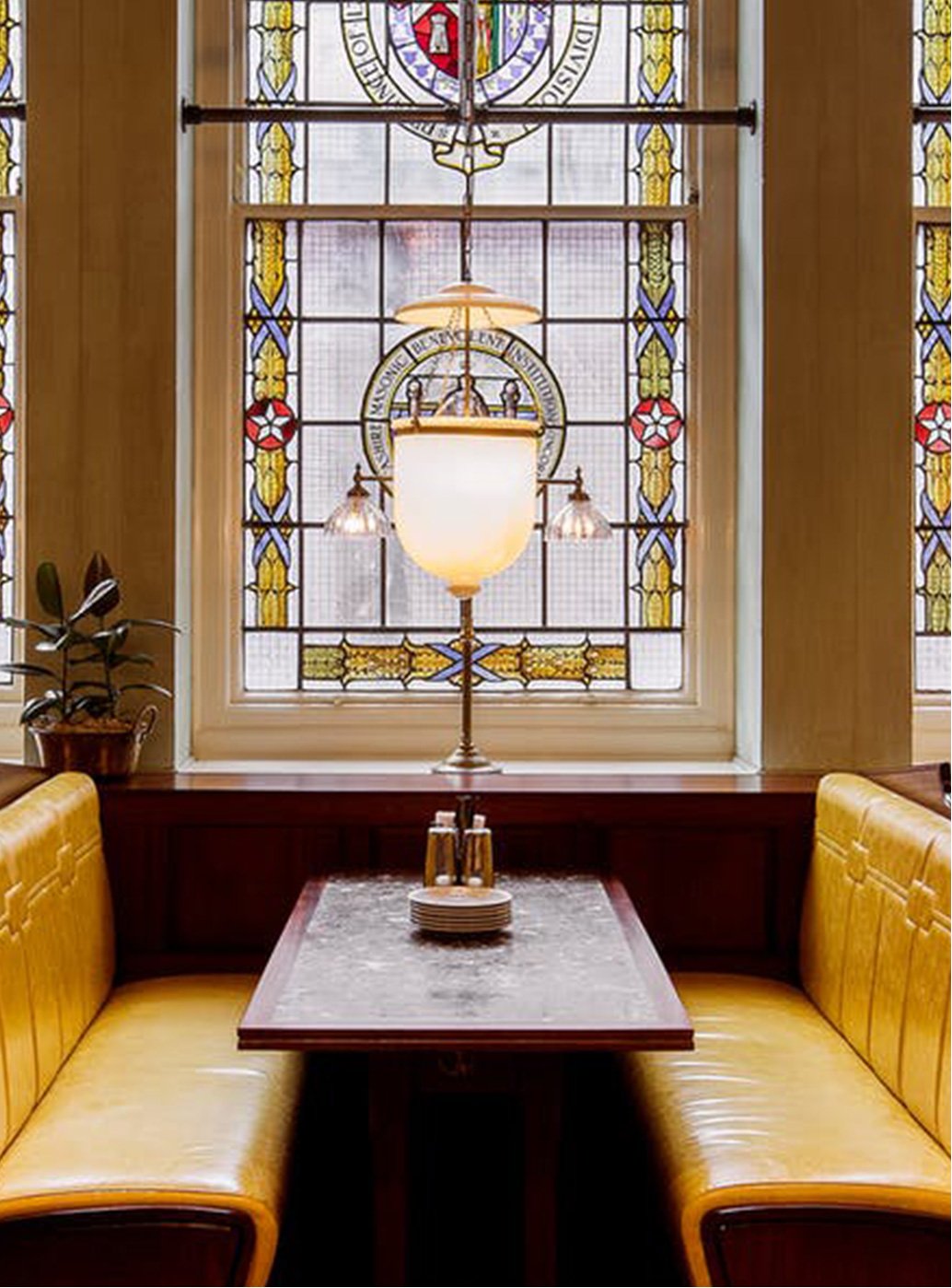 The stained glass window and yellow banquette leather sofa of Dishoom in Manchester.