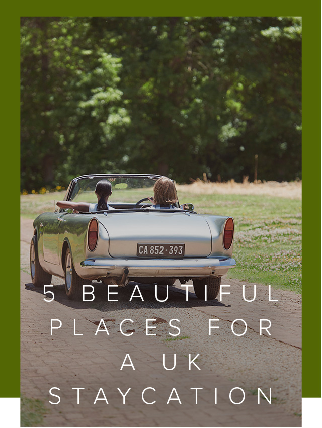 Two women drive away ina vintage car on a sunny day.