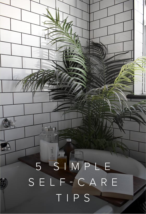 A serene white bathroom with white metro tiles and black grout, a green leafy plan and an array of luxurious bath products.