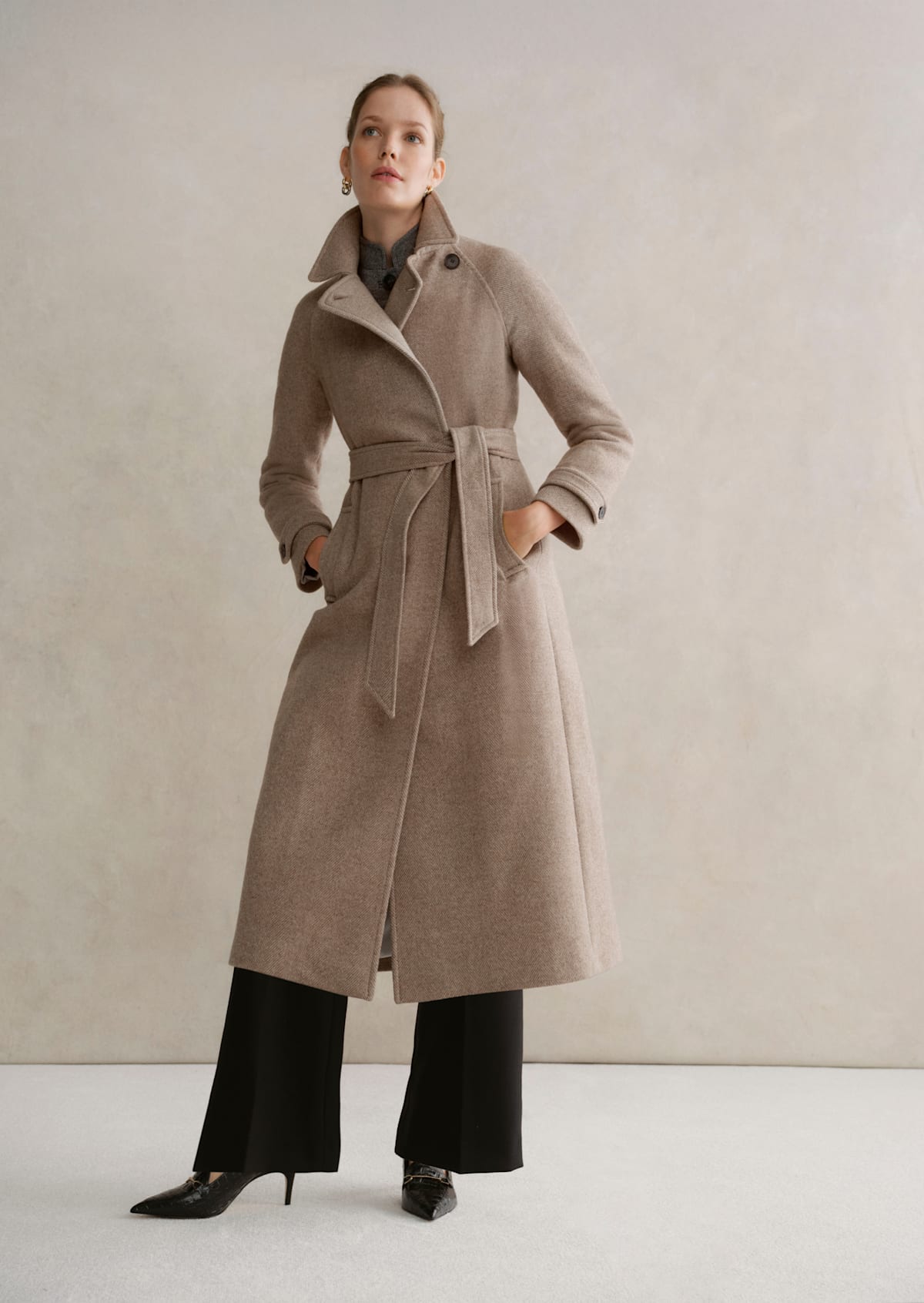 A gallery of two images displaying a model wearing a beige tailored coat.
