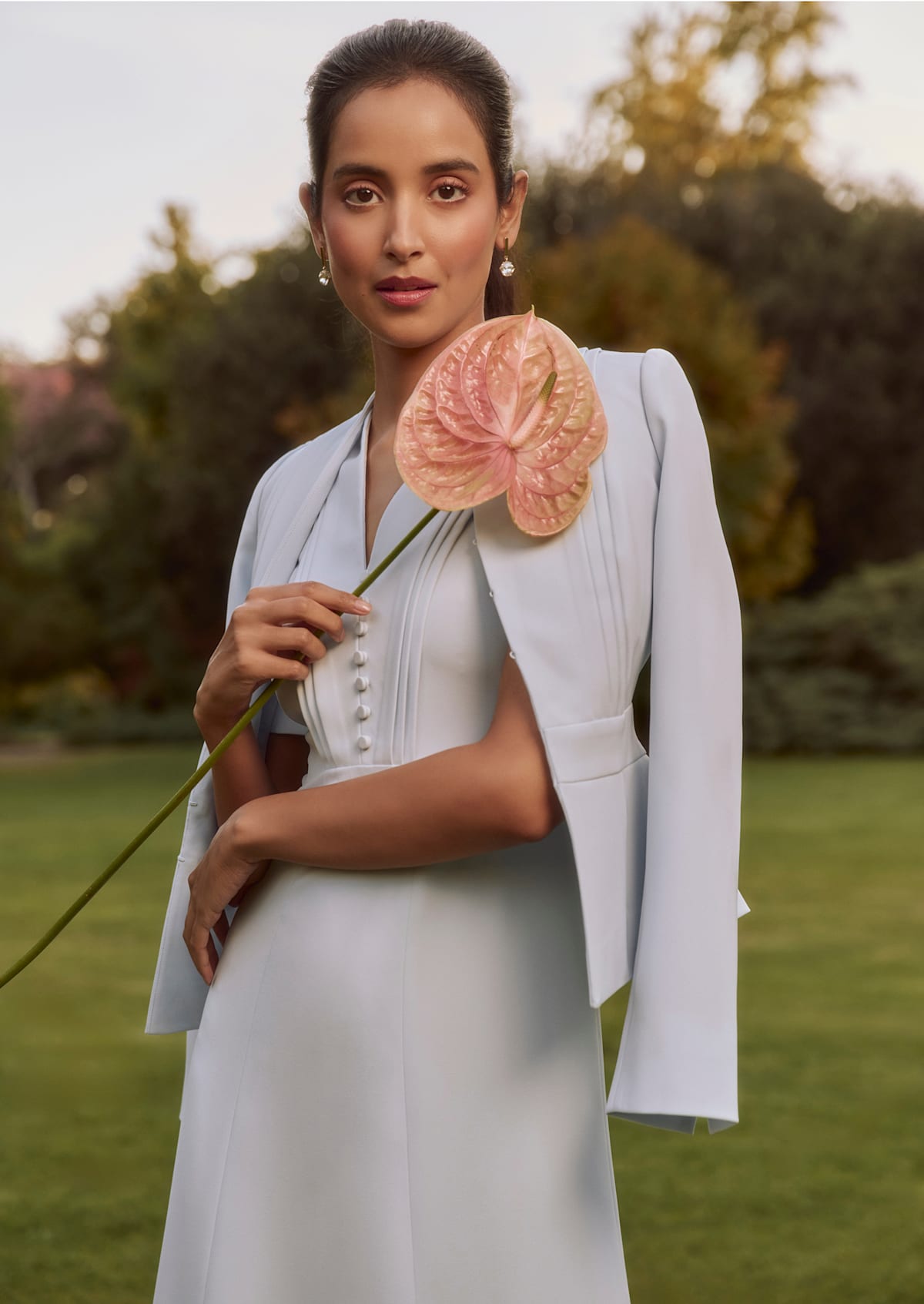 An image of a model wearing a pale blue dress and coordinating occasion jacket from Hobbs, while holding a flower.