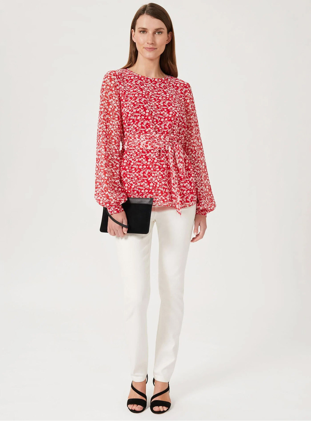 Model wears a floral print blouse and white jeans with heels and a clutch.