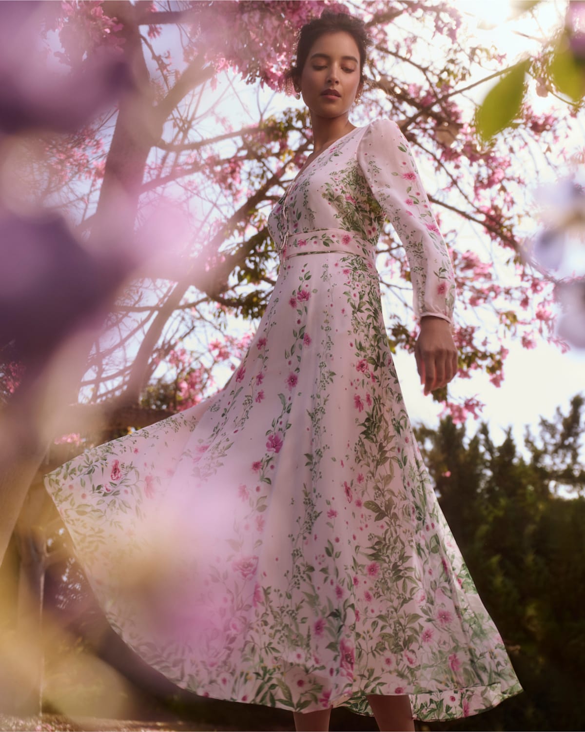 An image of a Hobbs model wearing an all-pink occasion outfit in front of a floral backdrop.