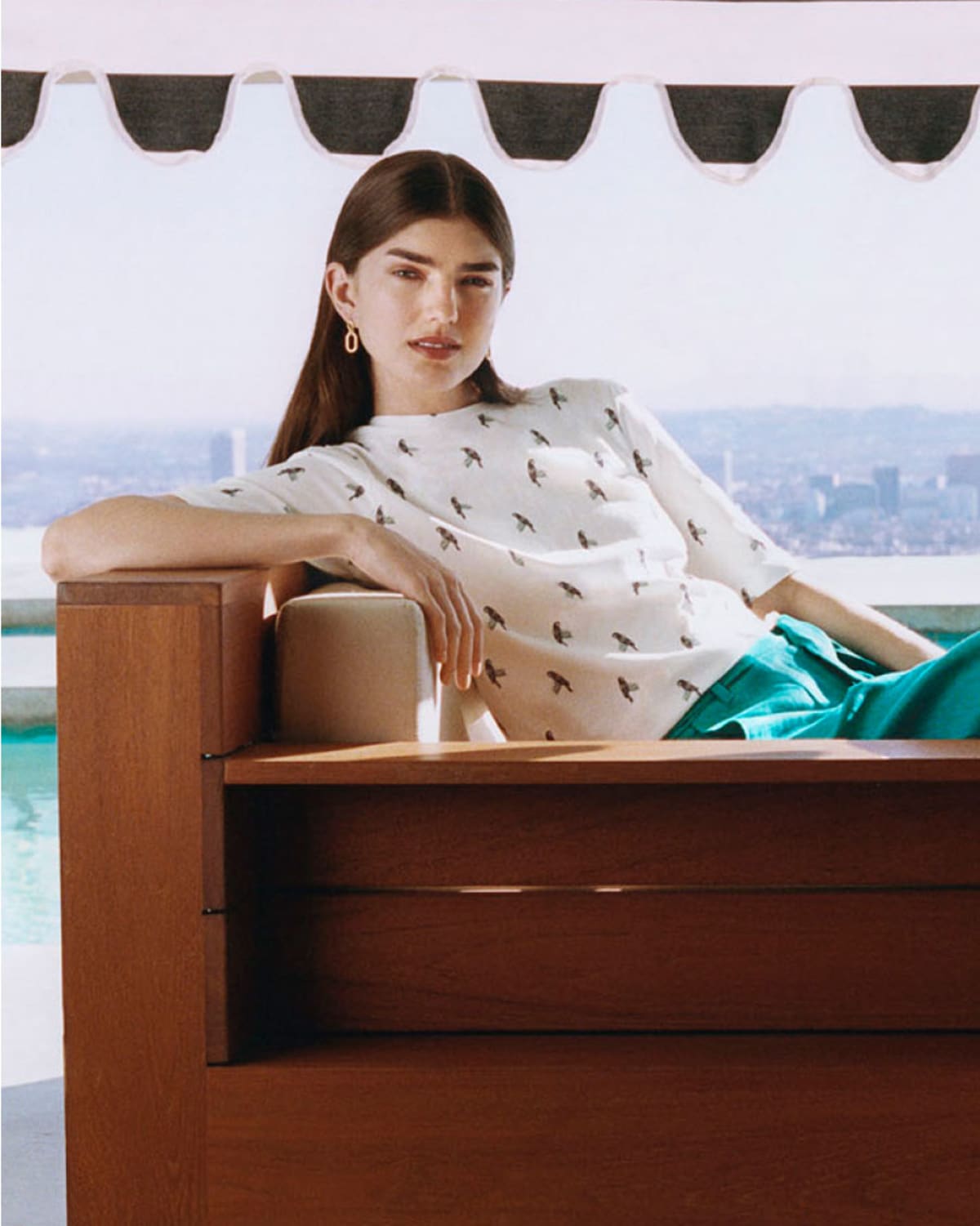 Image of model pictured lounging in the sunshine, wearing a red linen jumpsuit.