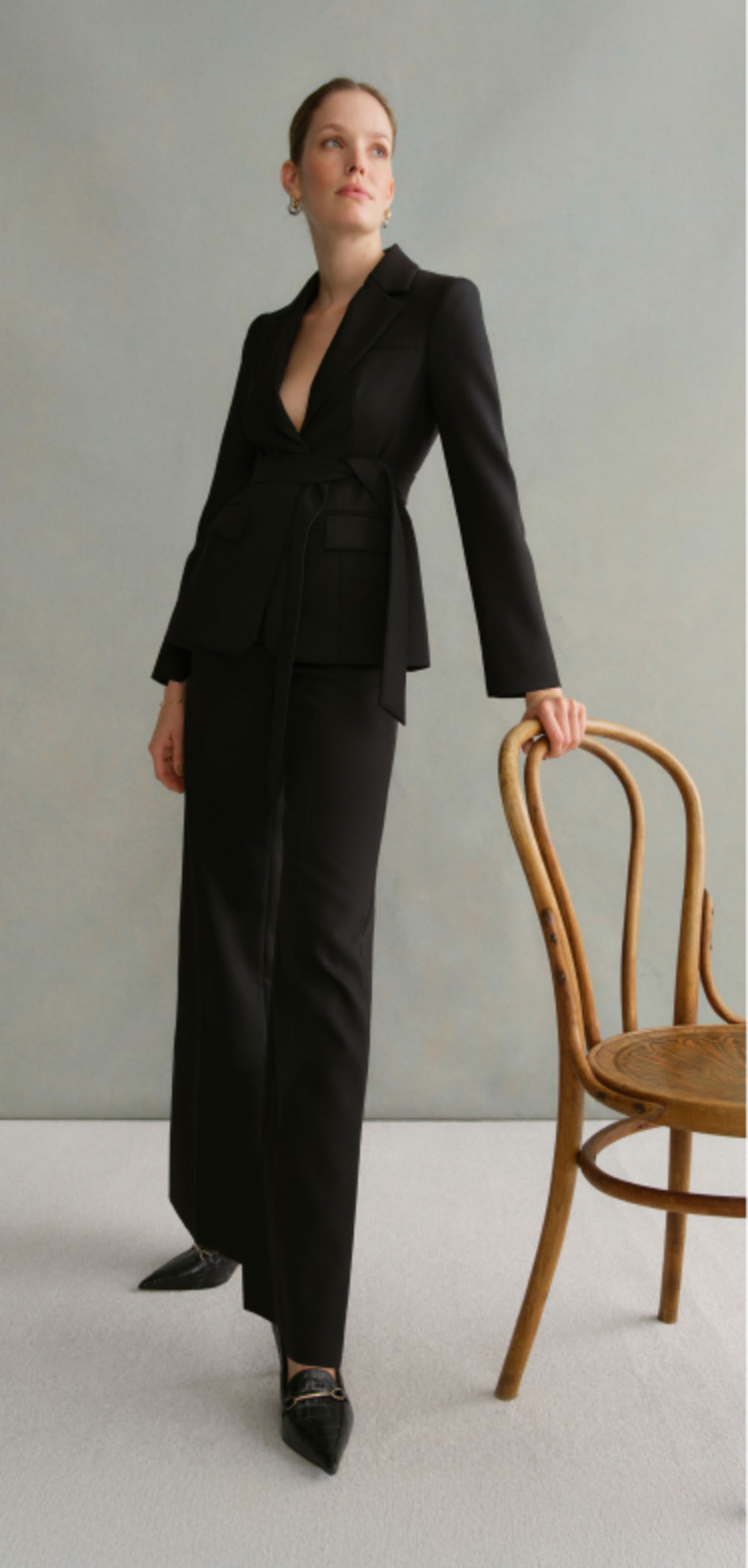 A gallery of four images including one image of a model wearing a women’s black suit, and three smaller images displaying details of the blazer.