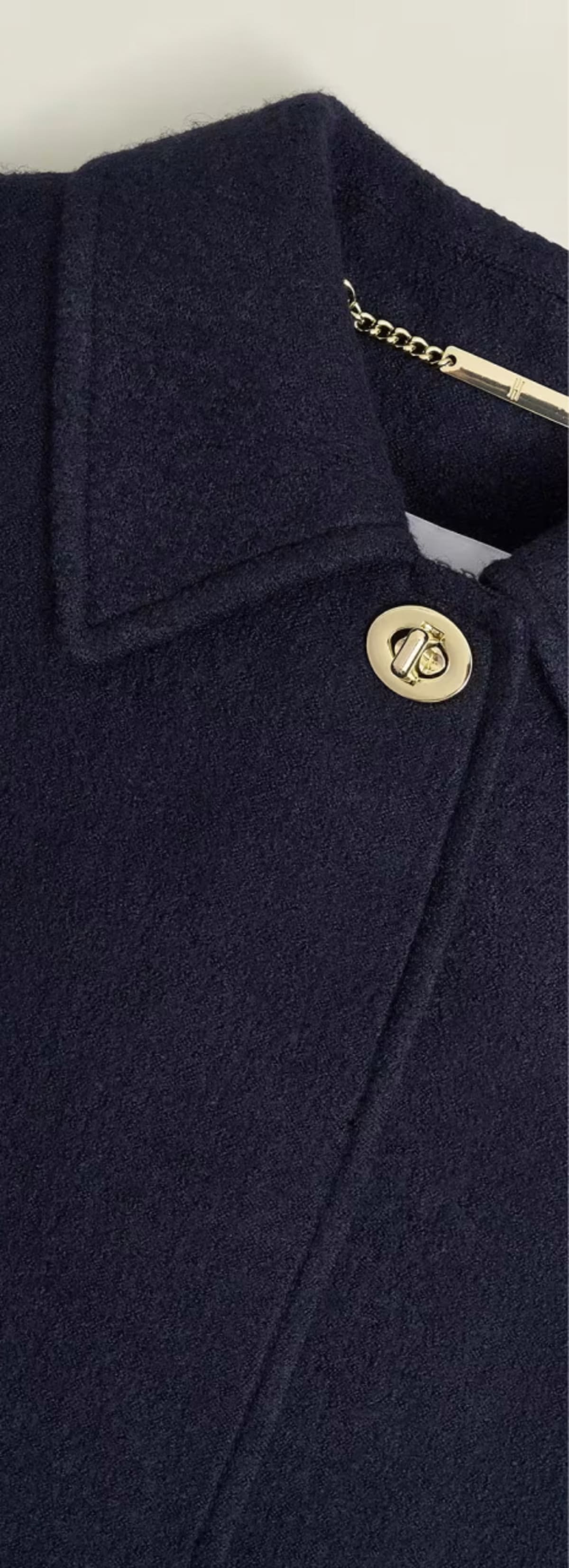 A gallery of four images including one image of a model wearing a navy coat, and three smaller images displaying details of the coat.