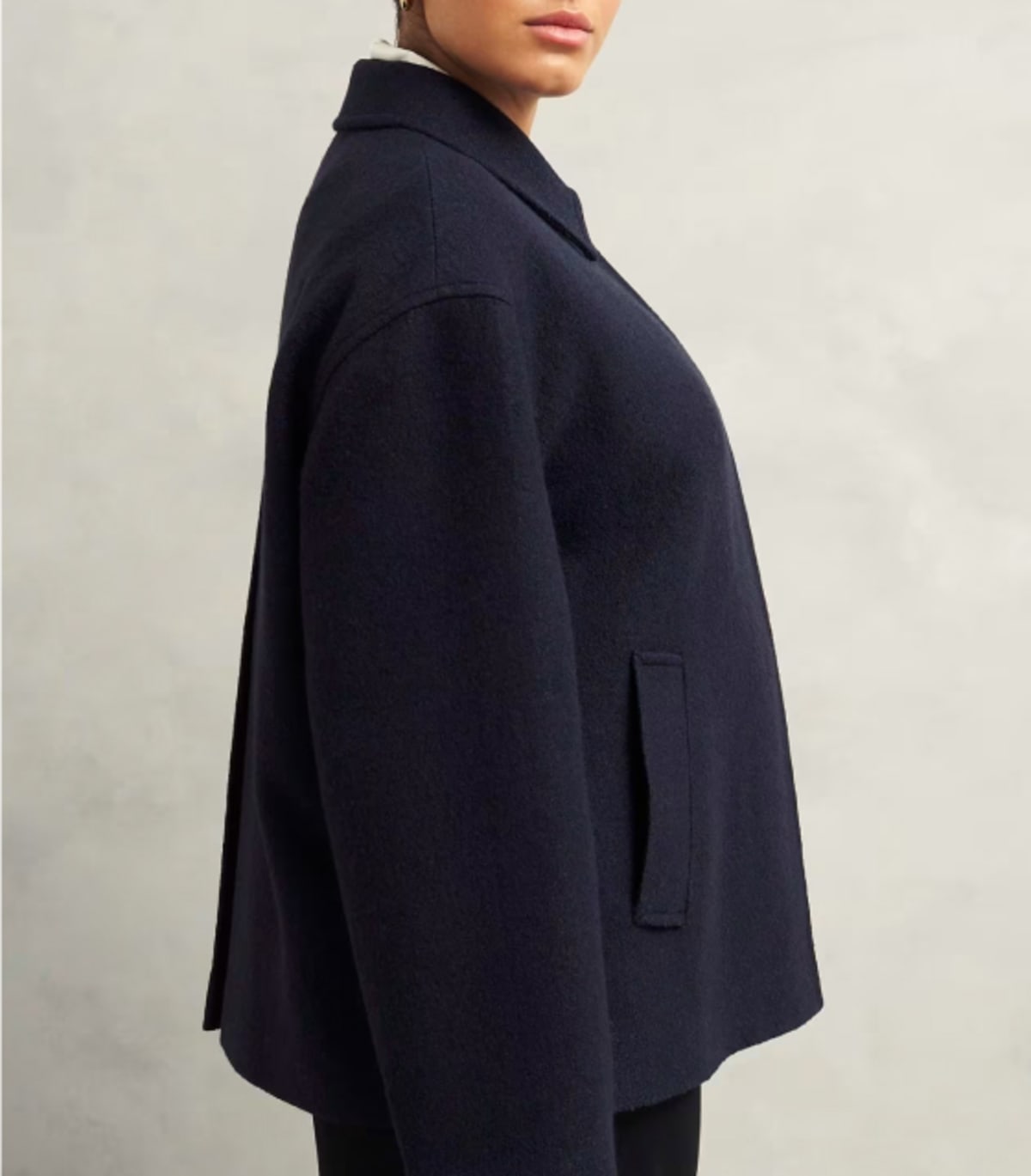 A gallery of four images including one image of a model wearing a navy coat, and three smaller images displaying details of the coat.