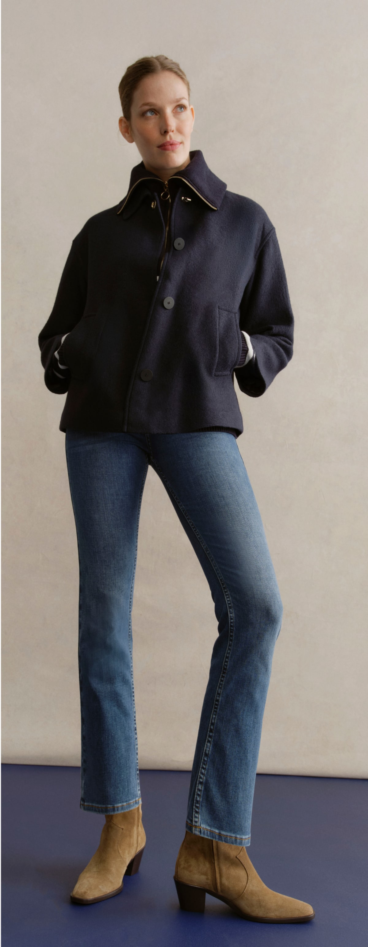 A gallery of four images including one image of a model wearing a navy coat, and three smaller images displaying details of the coat.