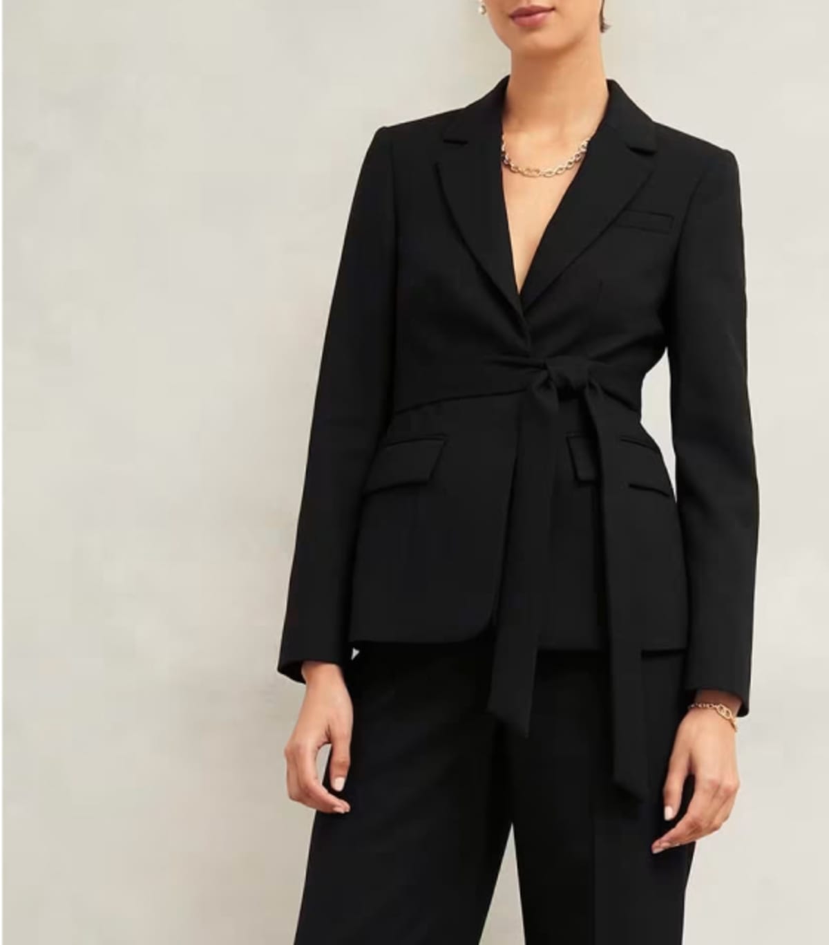 A gallery of four images including one image of a model wearing a women’s black suit, and three smaller images displaying details of the blazer.