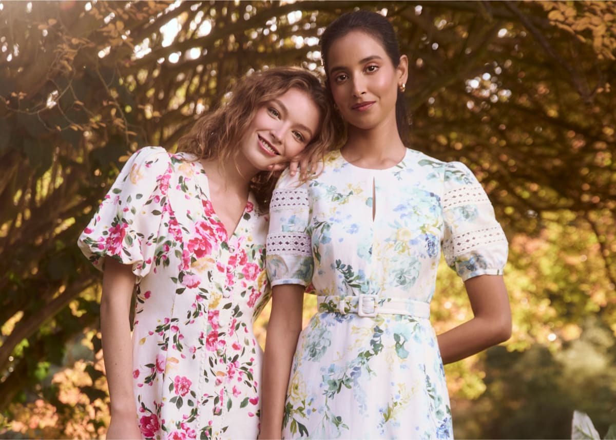 An image of two Hobbs models wearing floral midi dresses in a sunny backdrop.