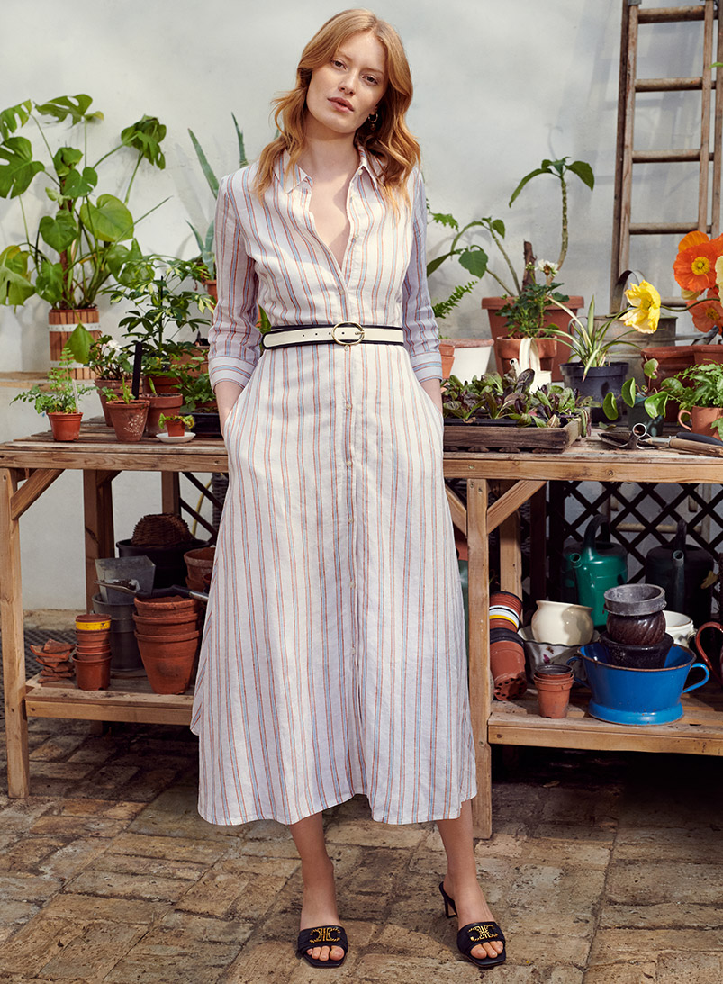 Model wearing a Hobbs striped linen shirt dress with black sandals in a garden.
Alt text: Model wearing a Hobbs t-shirt with 'Hello Summer' slogan in a garden.
